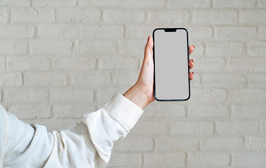 Cellphone with blank screen held by woman's hand against white brick wall