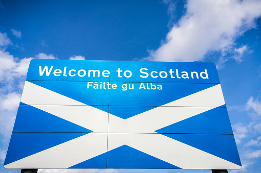 A large sign welcoming people to Scotland at the Scotland/England border, with text in English and Gaelic.