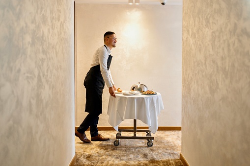 A waiter in uniform delivering a tray with food in a room to a hotel guest