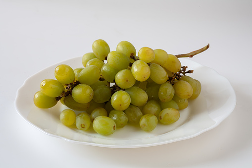 On the table in a plate is a bunch of grapes. On a white background.