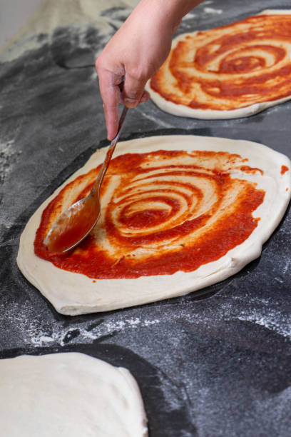 pizzaiolo spreads tomato sauce onto pizza - restaurant pasta italian culture dinner imagens e fotografias de stock