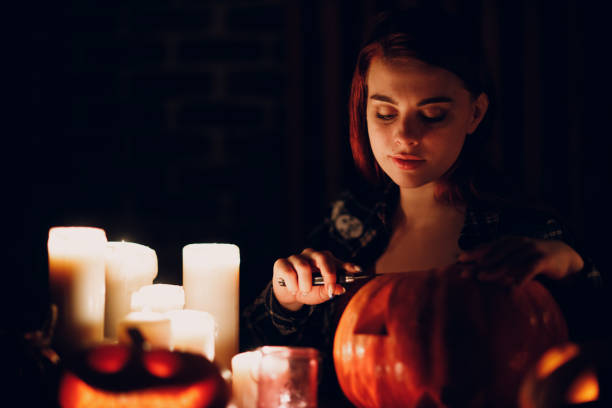 Young woman making Halloween pumpkin Jack-o-lantern. Female hands cutting pumpkins with knife. Young woman making Halloween pumpkin Jack-o-lantern with candles in dark. Female hands cutting pumpkins with knife halloween pumpkin human face candlelight stock pictures, royalty-free photos & images
