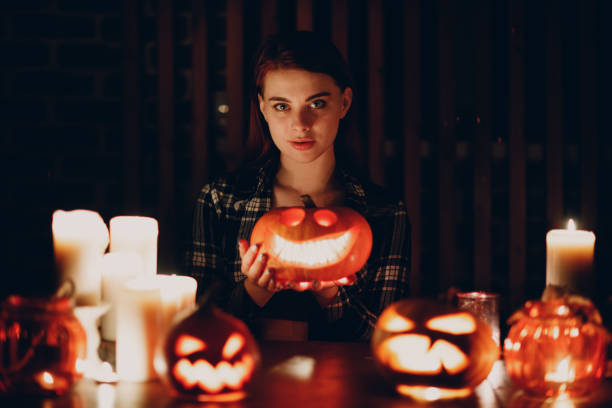 Young woman making Halloween pumpkin Jack-o-lantern. Female hands cutting pumpkins with knife. Young woman making Halloween pumpkin Jack-o-lantern with candles in dark halloween pumpkin human face candlelight stock pictures, royalty-free photos & images