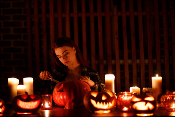 Young woman making Halloween pumpkin Jack-o-lantern. Female hands cutting pumpkins with knife. Young woman making Halloween pumpkin Jack-o-lantern with candles. Female hands cutting pumpkins with knife halloween pumpkin human face candlelight stock pictures, royalty-free photos & images