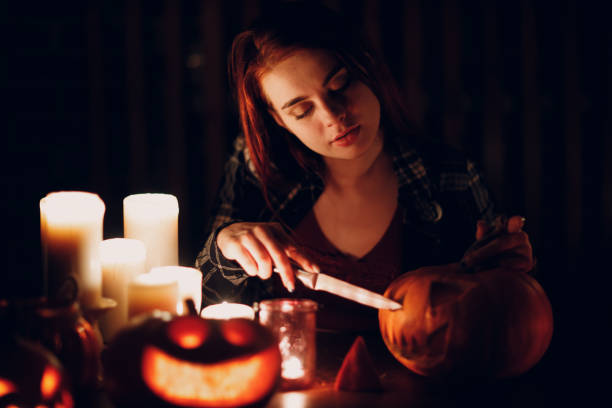 Young woman making Halloween pumpkin Jack-o-lantern. Female hands cutting pumpkins with knife. Young woman making Halloween pumpkin Jack-o-lantern with candles in dark. Female hands cutting pumpkins with knife halloween pumpkin human face candlelight stock pictures, royalty-free photos & images