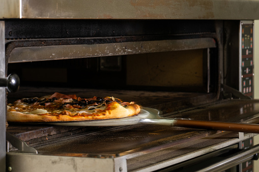Skilled pizzaiolo carefully removes freshly baked pizzas from the oven in a bustling pizzeria. Authentic Italian craftsmanship captured in a single shot.