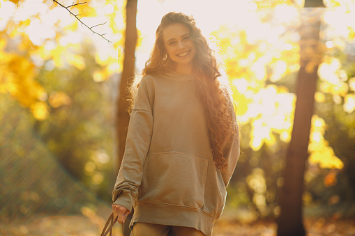 Smiling young woman walking in autumn forest with the yellow leaves at sunset