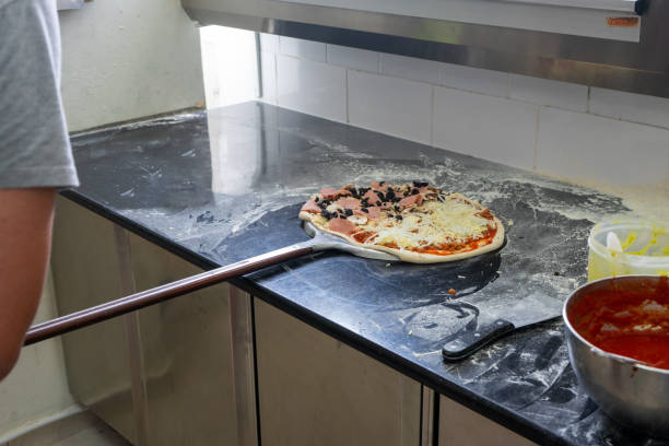 Skilled pizzaiolo carefully removes freshly baked pizzas from the oven in a bustling pizzeria. Authentic Italian craftsmanship captured in a single shot.