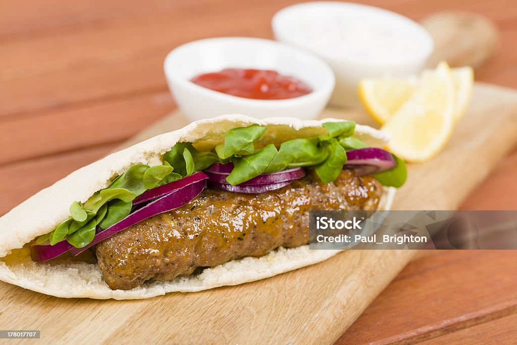 Seekh Kebabs in Pita Bread Grilled minced meat kebabs in a flatbread with salad served with lemon wedges, chili sauce and cucumber, onion and yoghurt raita. Rustic outdoors setting. Afghan Ethnicity Stock Photo