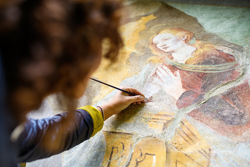 Professional restorer restoring antique chapel fresco in Italy