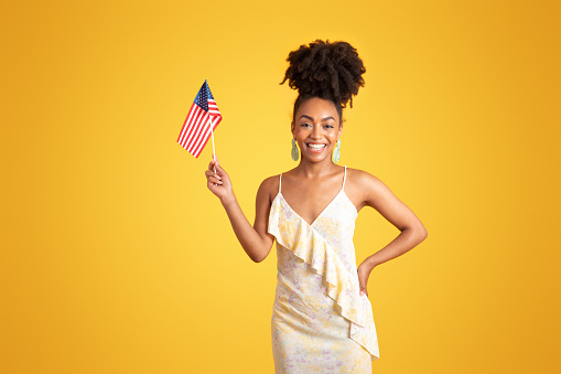Smiling millennial african american lady showing USA flag, isolated on yellow background, studio. Ad and offer, education, learn english language, exchange study at university