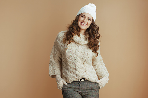 Hello winter. Portrait of smiling modern woman in beige sweater, mittens and hat isolated on beige.