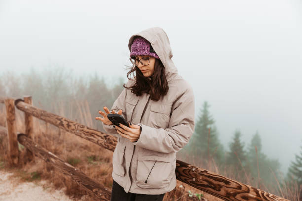 istock A young female hiker walks in nature and searches for a path on her mobile phone map. She is in a forest where it's foggy, cold, and windy - Stock Photo 1780260138
