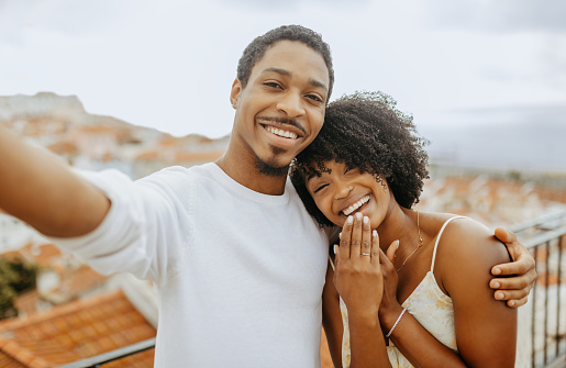 Happy satisfied millennial african american man hugging woman with ring, making selfie, video call in city, outdoor. Lifestyle, love and relationship, wedding, engagement, blog