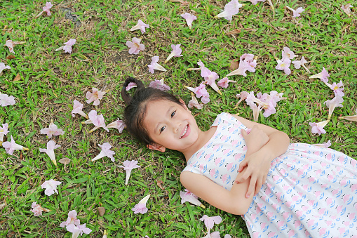 Happy little girl lying on green grass with fall pink flower in the garden outdoor.