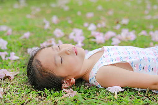 Close up little girl sleeping on green grass with fall pink flower in the garden outdoor.