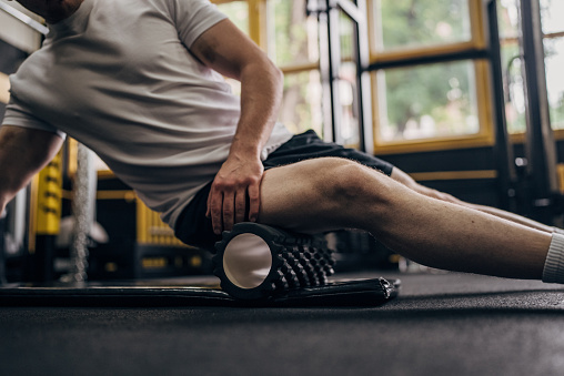 Man massaging his leg muscles with foam roller in the gym.