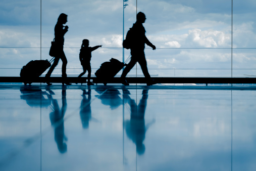 Sihouette of young family with luggage walking at airport, girl pointing at the window