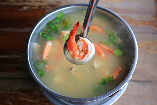 Spicy shrimp soup or Tom yum goong hot and sour in pot on wood table. Thai traditional cuisine.