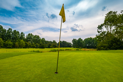 golf course with yellow flag on 18th hole at cloudy sky
