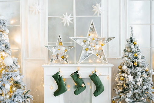 Christmas decor of the white fireplace in the living room. Fairy stars and socks for Santa Claus