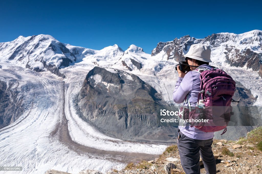 Switzerland travel - female hiker photographing the view of the Grenz glacier Switzerland Travel - Senior Asian woman hiking and photographing the Gorner Glacier from Gornergrat in Zurich 60-69 Years Stock Photo