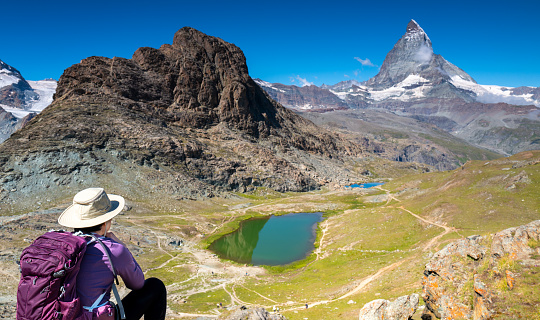 Switzerland travel: Female hiker sitting and enjoying the view of Riffelsee and the Matterhorn in the mountains of Zermatt.