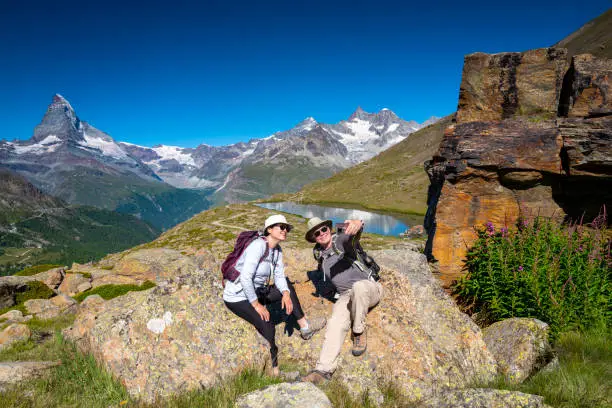 Senior couple taking a selfie picture while on a break from hiking near Stellisee in Zermatt, Switzerland with views of the Matterhorn in the background.