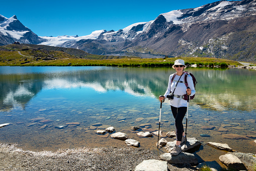 Senior woman hiking the Swiss alps, stands near lake Stellisee , Switzerland with views of snowcapped mountains and glaciers in the background.