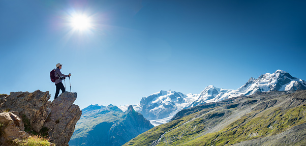 Switzerland travel - woman hiking the Swiss alps near Zermatt enjoys the view from the edge of mountain top.