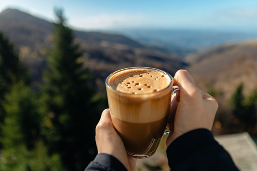 The girl is enjoying the view of the mountain range while holding a cup of coffee in her hand - Stock Photo