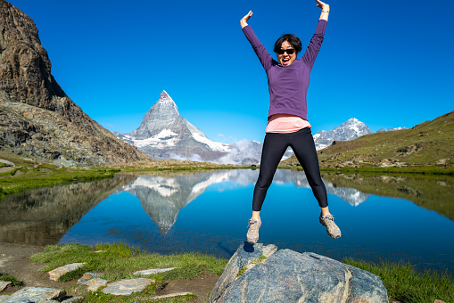 Switzerland Travel - Senior woman jumping for joy, hiking the Swiss Alps near the Matterhorn at Riffelsee