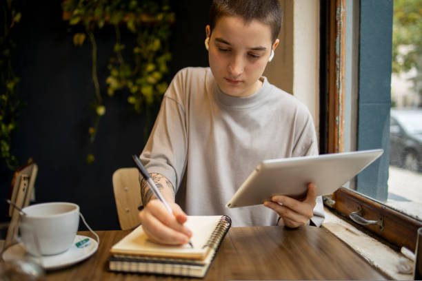 istock Latin transgender generation z student using mobile phone, digital tablet at the bar. He is using earphones for video call 1780337989
