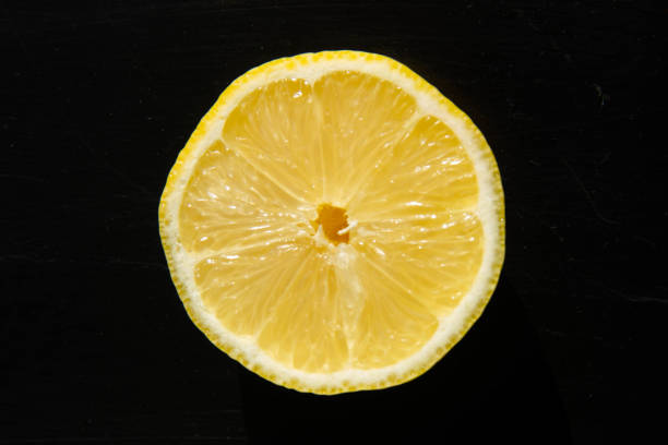 horizonatl studioaufnahme von einer hälfte eines runden, in scheiben geschnittenen frischen vitamins. gelbe zitronenfrucht auf schwarzem strukturiertem hintergrund nahaufnahme, draufsicht - horizonatl stock-fotos und bilder