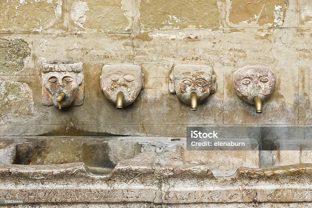 Human head fountain Ancient stone fountain with four faces with metal pipe in the mouth Cold Drink Stock Photo