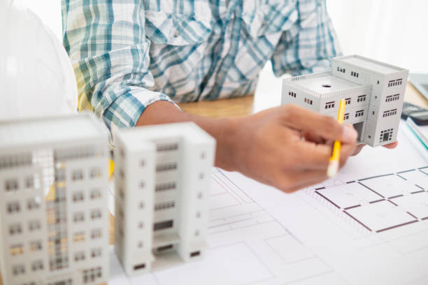 istock architect is preparing house model and construction plans on blueprints for construction engineering team to review before construction engineering team constructs building according to the drawings. 1780348959