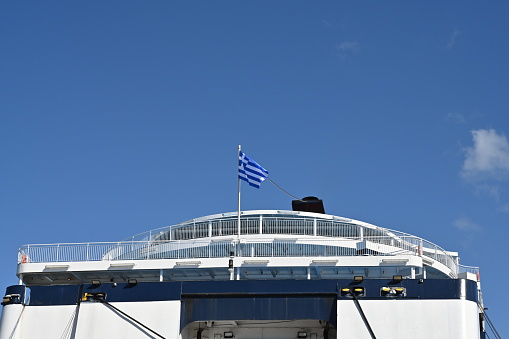 Heraklion, Greece 09 13 2023, Aft part of passenger ferry with blue and white hull and Greece flag on top is observed against clear sky. Vessel is moored in port of Heraklion in Crete.