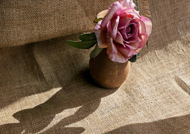still life with artificial rose in a clay vase on burlap fabric background