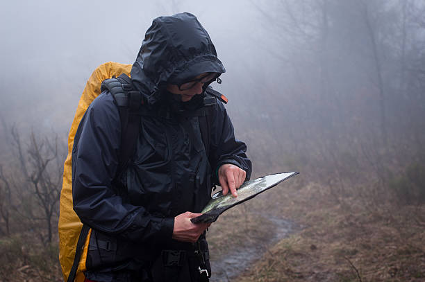 Man in raincoat and yellow backpack reviewing map in mist stock photo