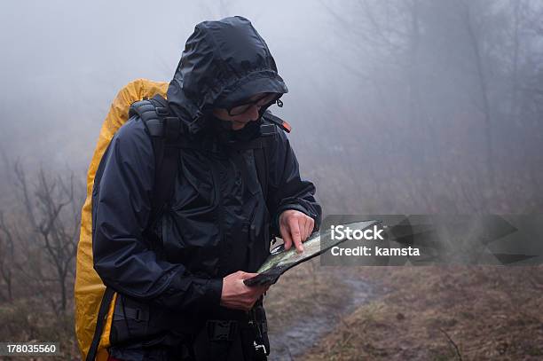 Man In Raincoat And Yellow Backpack Reviewing Map In Mist Stock Photo - Download Image Now