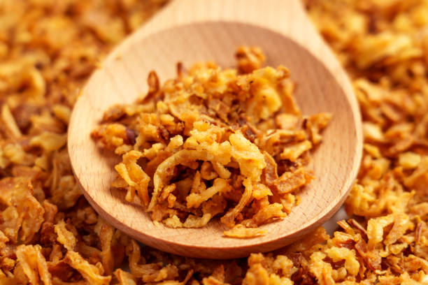 Crispy fried onions in wooden spoon. Roasted golden shallot flakes.