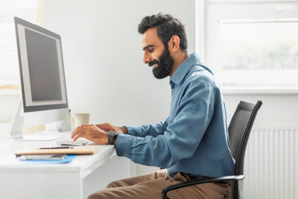 istock Happy bearded indian businessman sitting at worktable at office, typing on computer keyboard 1780363700