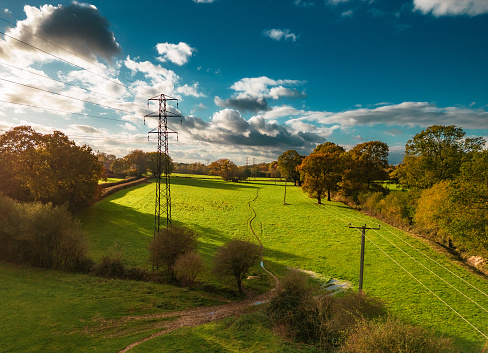 High angle view, taken by drone, depicting electricity pylons receding into the distance in a rural area of southeast England.