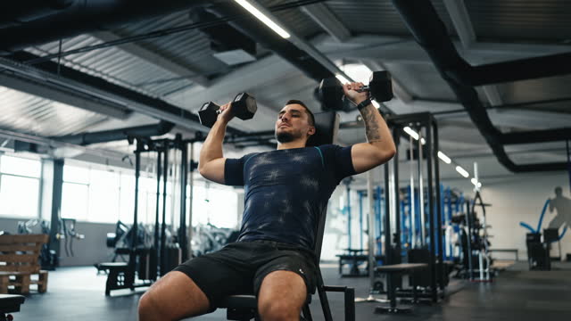 Young Muscular Man Endurance Exercising With Dumbbell to Pump Up Arm Muscles in Fitness Center
