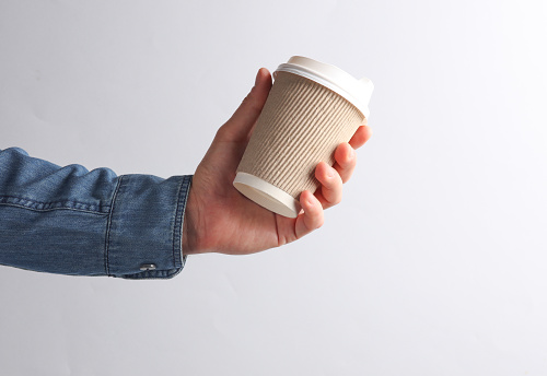 Man's hand in denim shirt holding craft paper coffee cup on a gray background