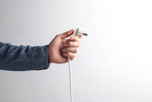 istock Man's hand in denim shirt holding electrical plug on a gray background 1780378319