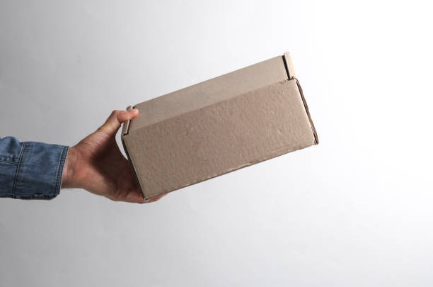 istock Man's hand in denim shirt holding cardboard postal box on gray background 1780378761