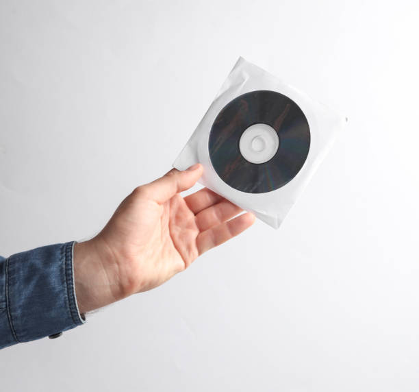 istock Man's hand in denim shirt holding CD disk in pack on a saucer, gray background 1780378804