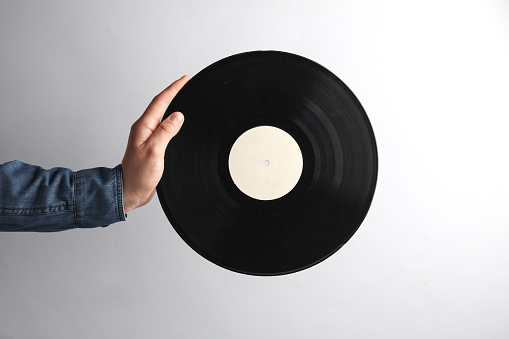 Man's hand in denim shirt holding vinyl record on gray background