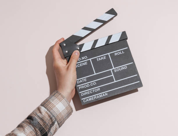 istock Man's hand in shirt holding clapperboard on beige pastel background with shadow. 1780379952